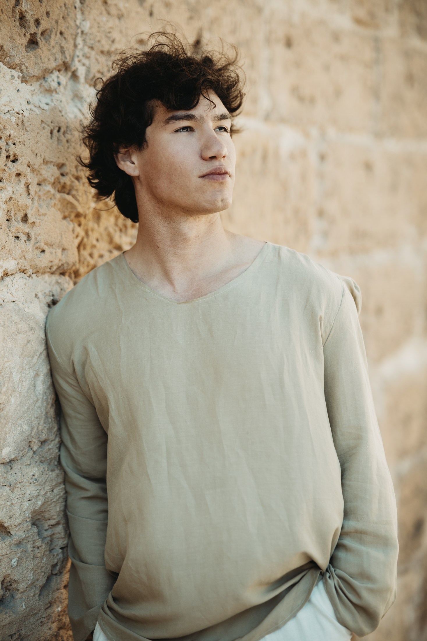 Portrait of a young man leaning against a sunlit stone wall.
