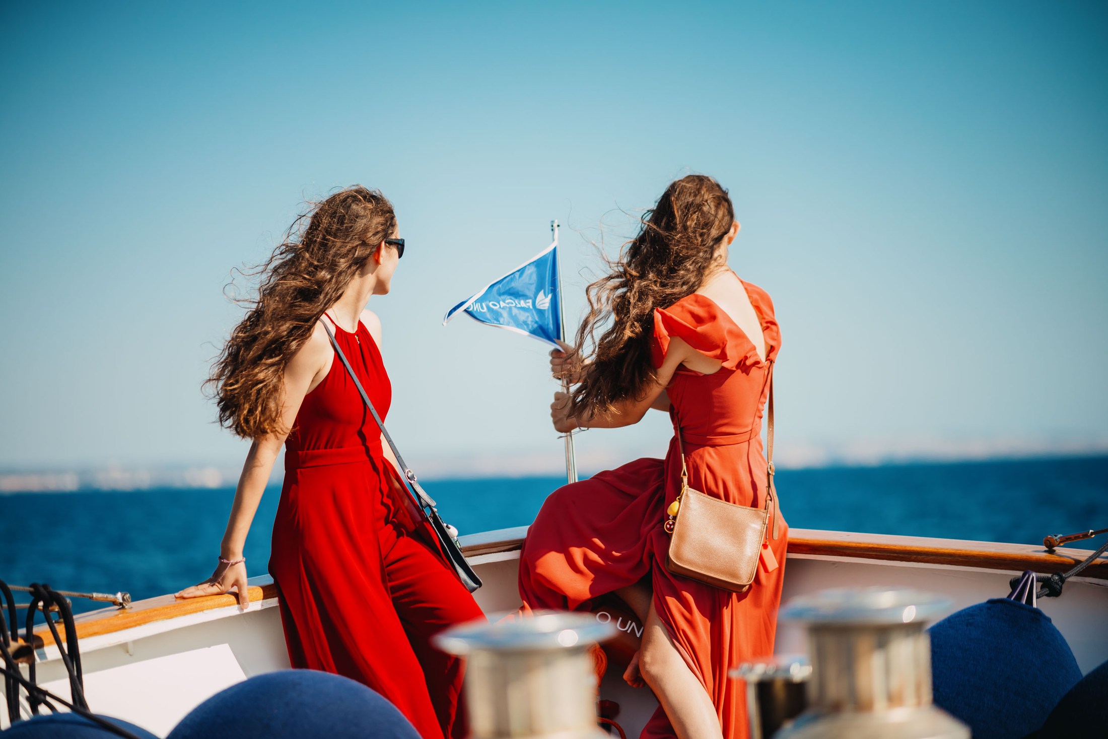 Two women in bright dresses standing on a boat by the sea.