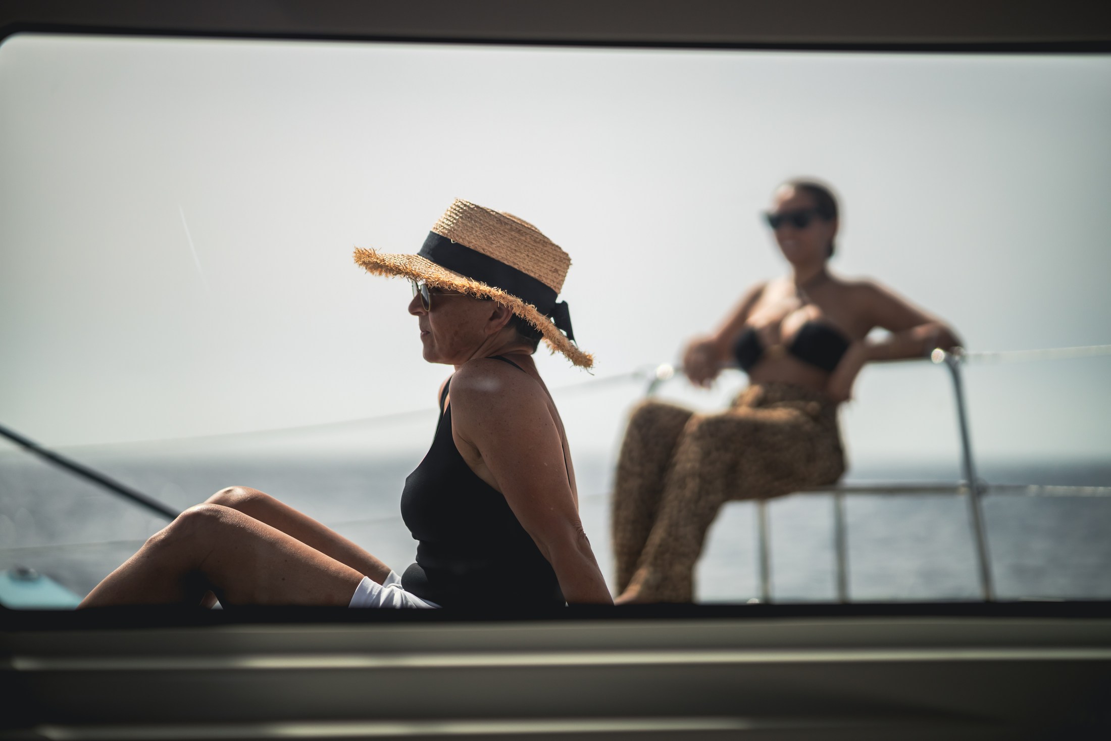 Woman in a sunhat relaxing on a boat with the sea behind her.
