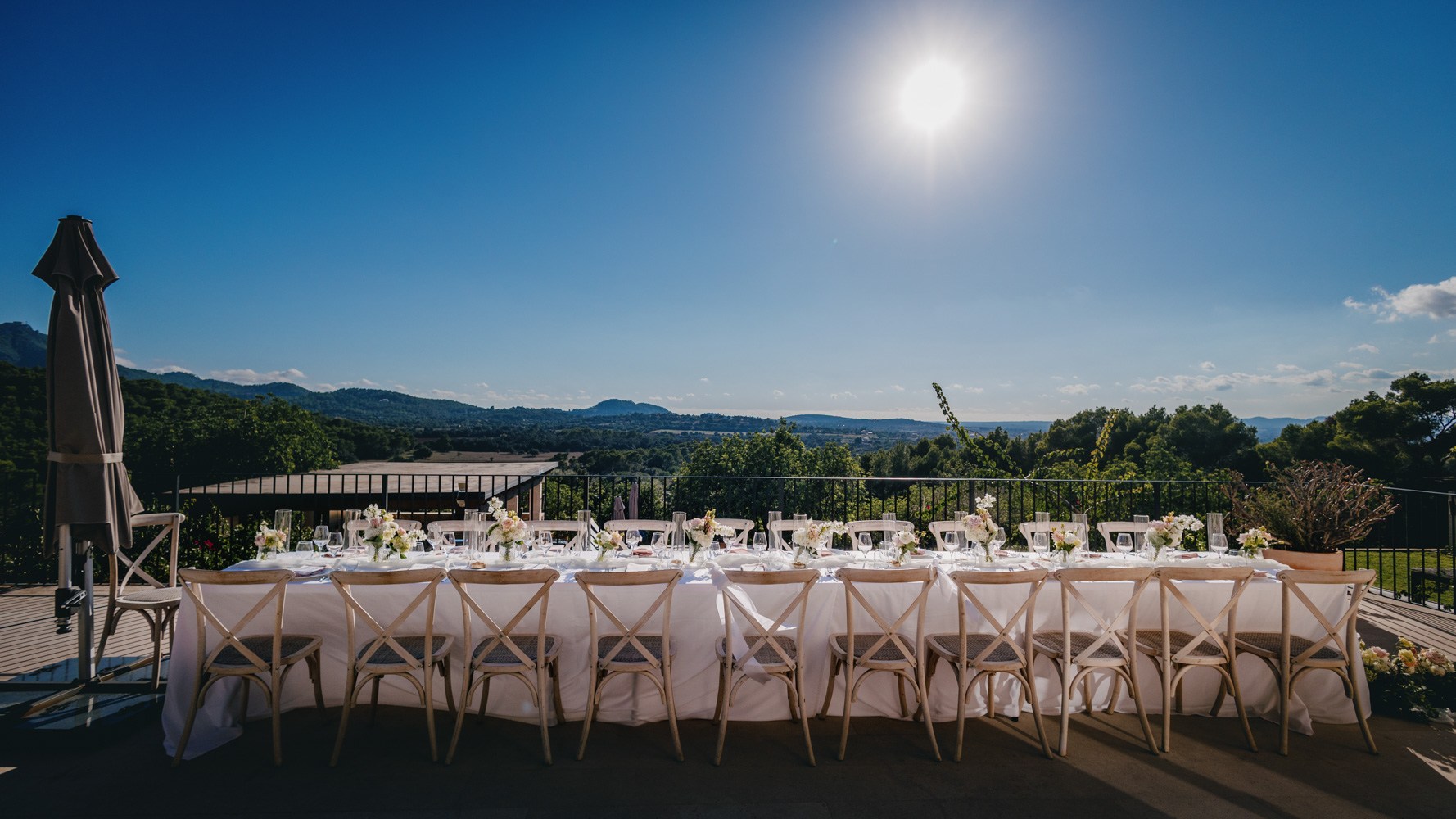 Long outdoor wedding table set for guests beneath the afternoon sun.