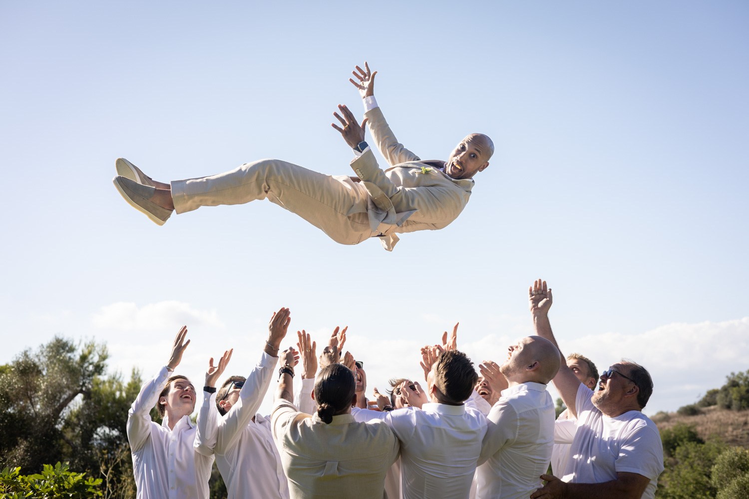 Wedding guests tossing the groom into the air.