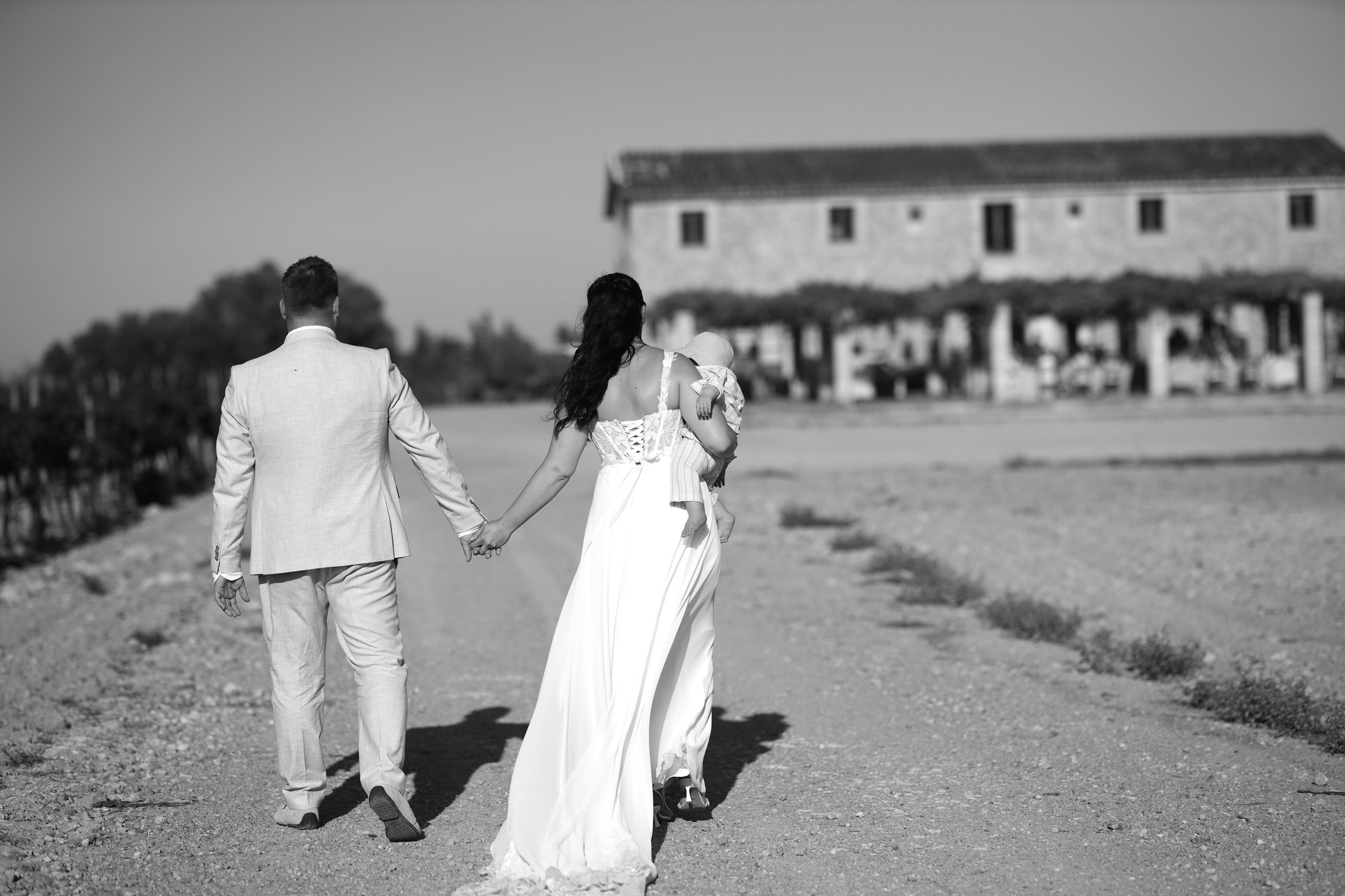 Bride and groom walking hand in hand toward a country venue.